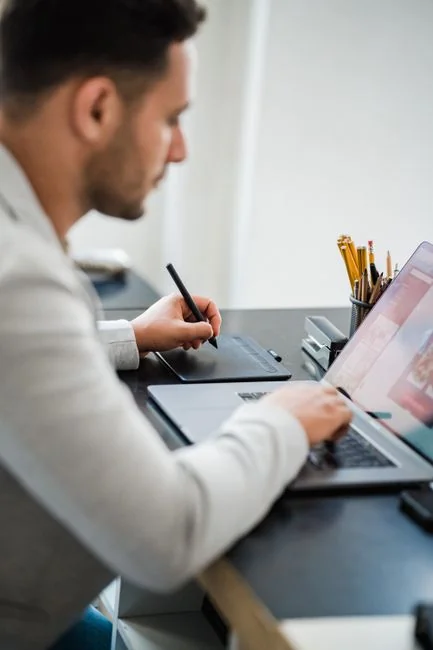 A fashion designer’s silhouette studying a mood board packed with fashion sketches and photographs.